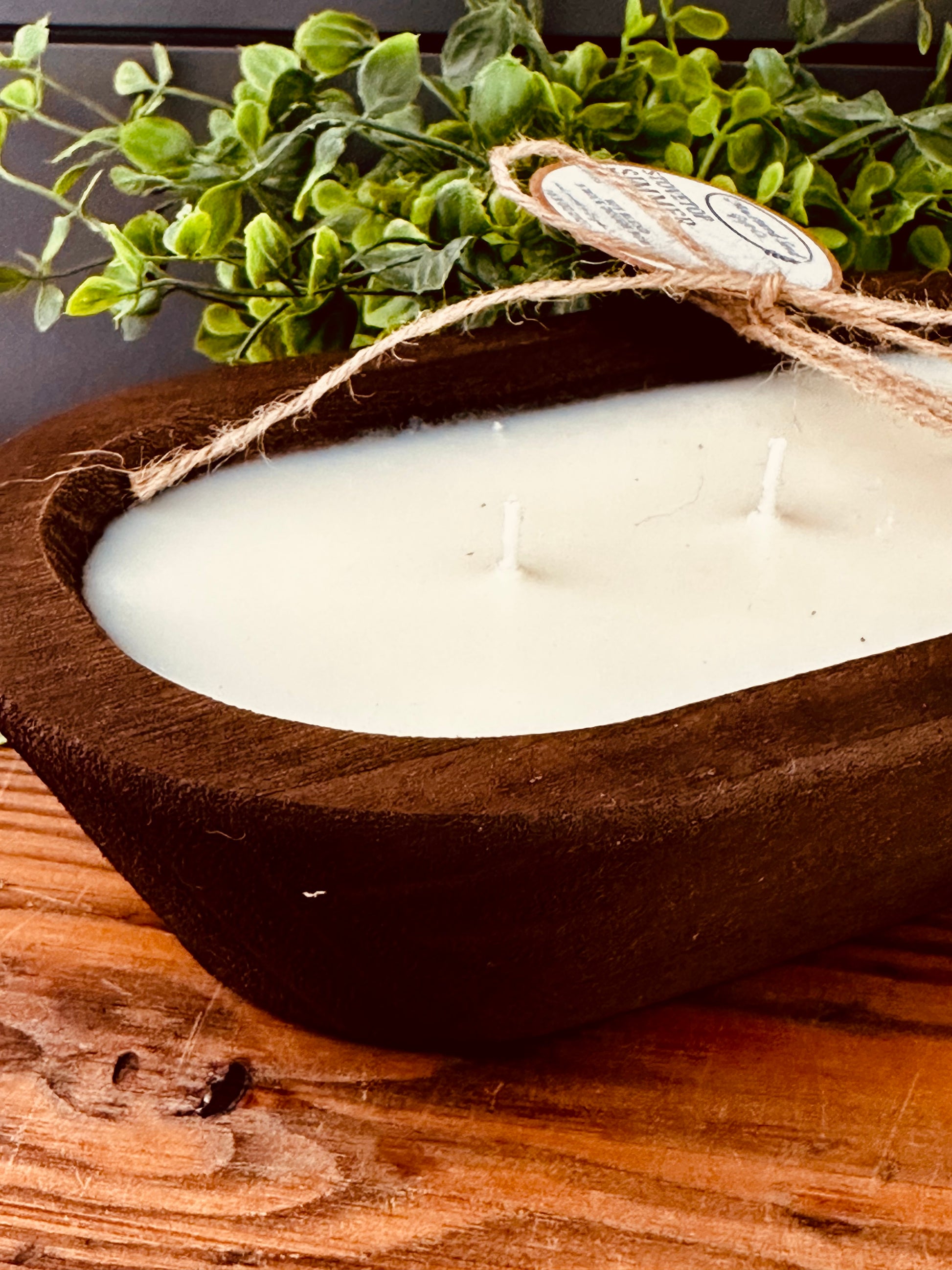 Candle in a wooden bowl with a plant in the background
